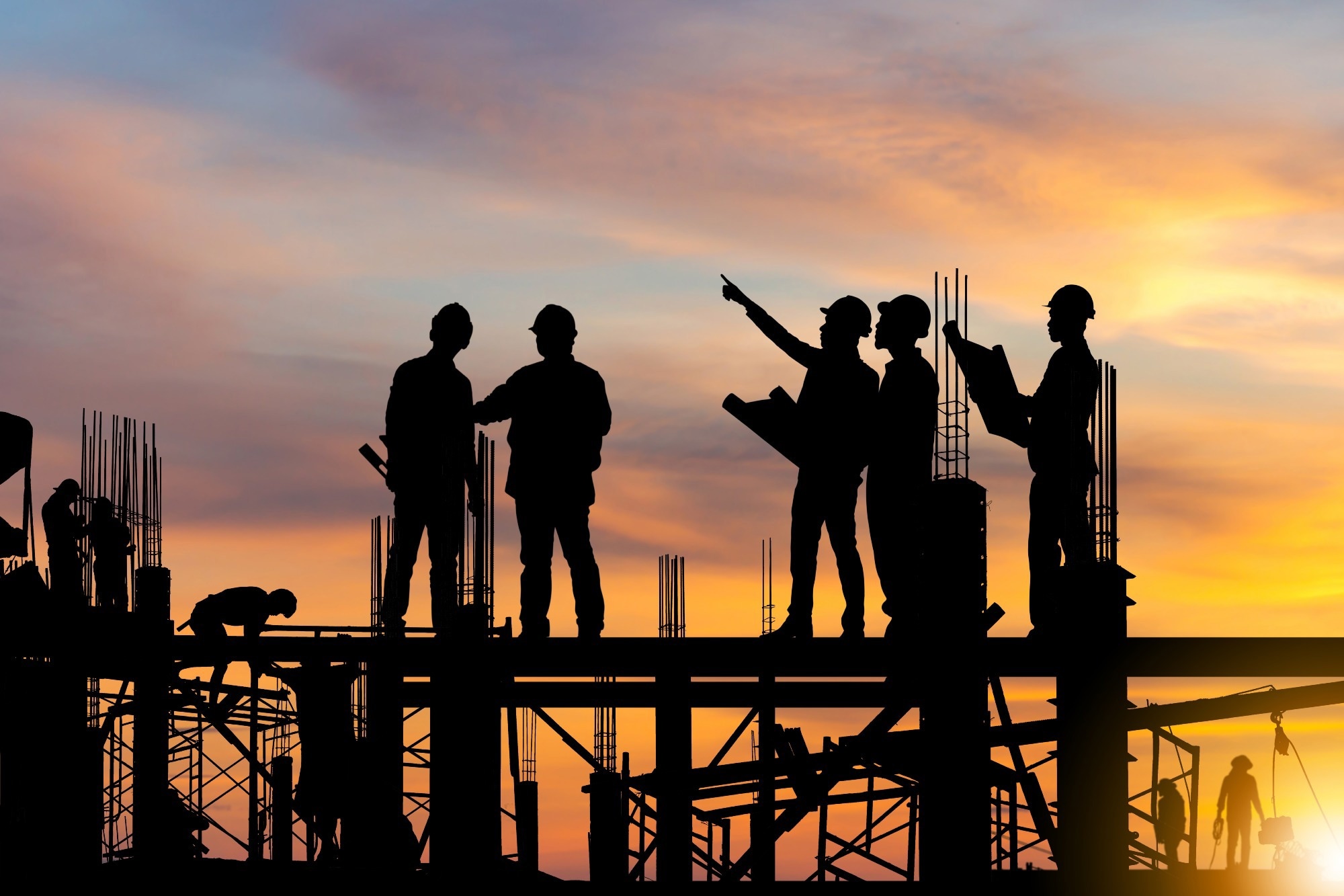 Silhouette of Engineer and worker on building site, construction site at sunset in evening time.