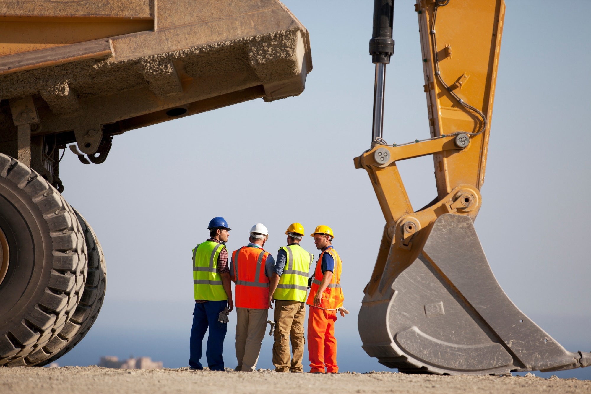 Workers talking by machinery at construction site.