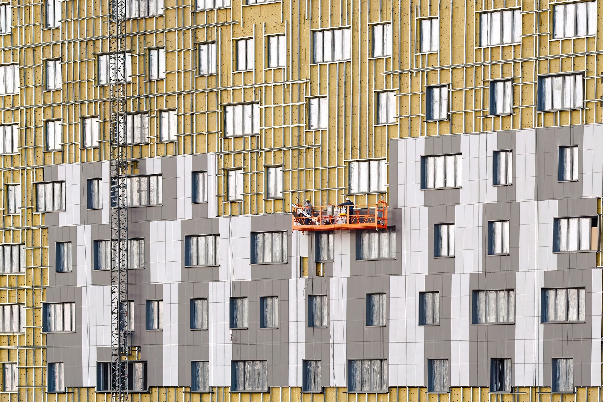 Man on suspended platform insulating wall facade of residential building.