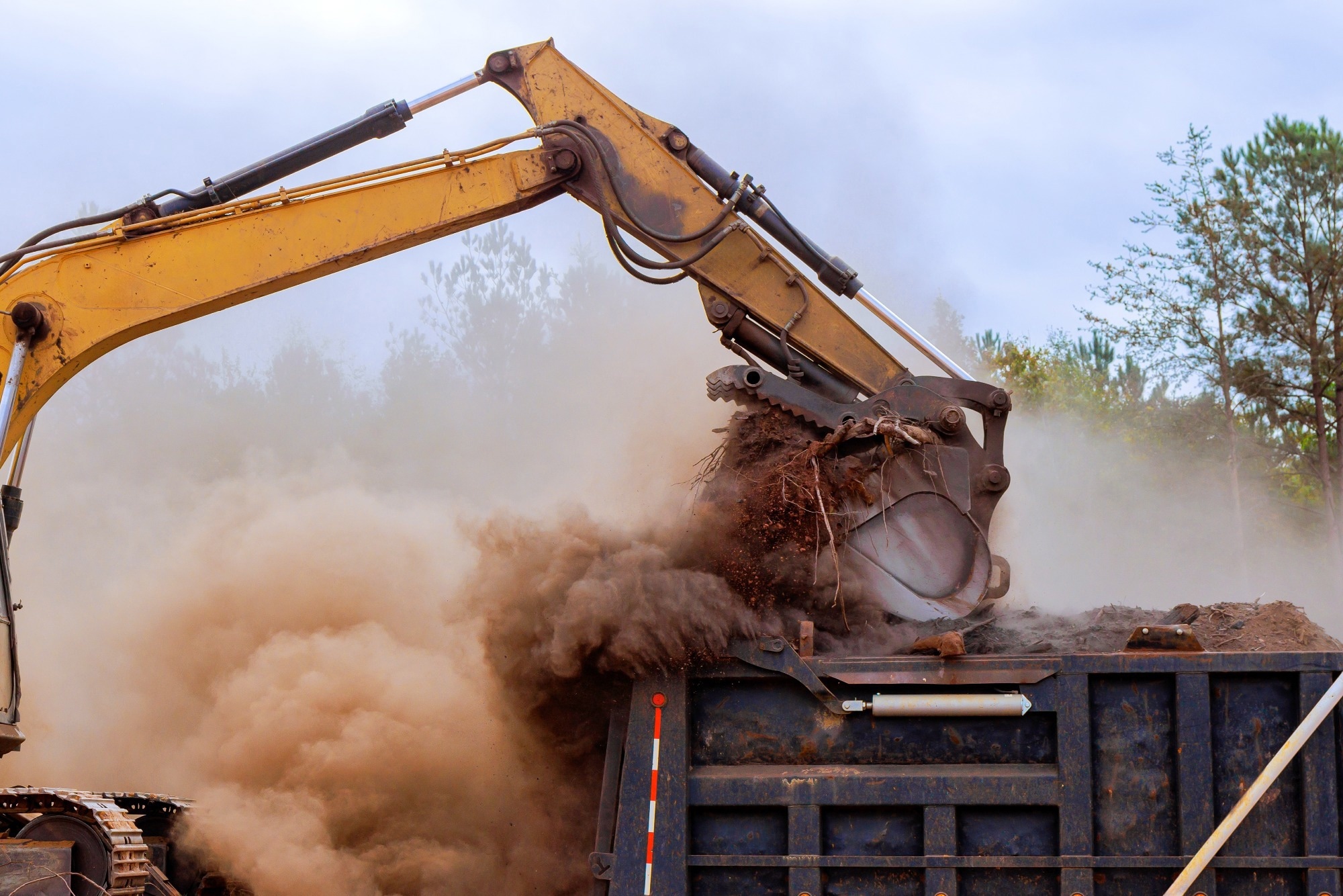 Heavy machinery lifts dirt, debris at construction site while dust clouds rise into air on works day.