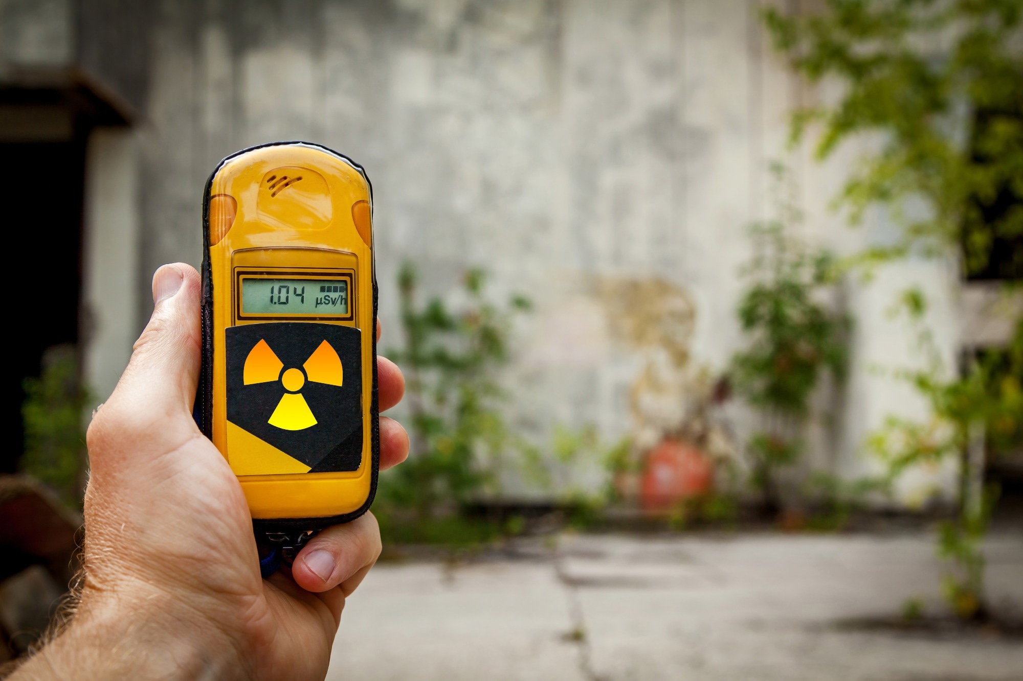 A man holding a yellow instrument for measuring a level of radiation on the background of an old stone wall.