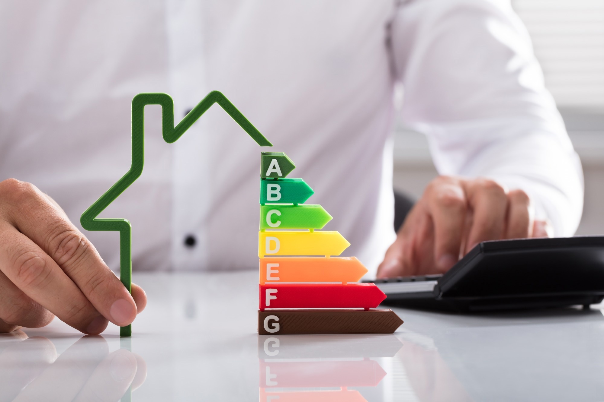 Close-up of a businessman using calculator holding outline of house model with energy efficiency rate.