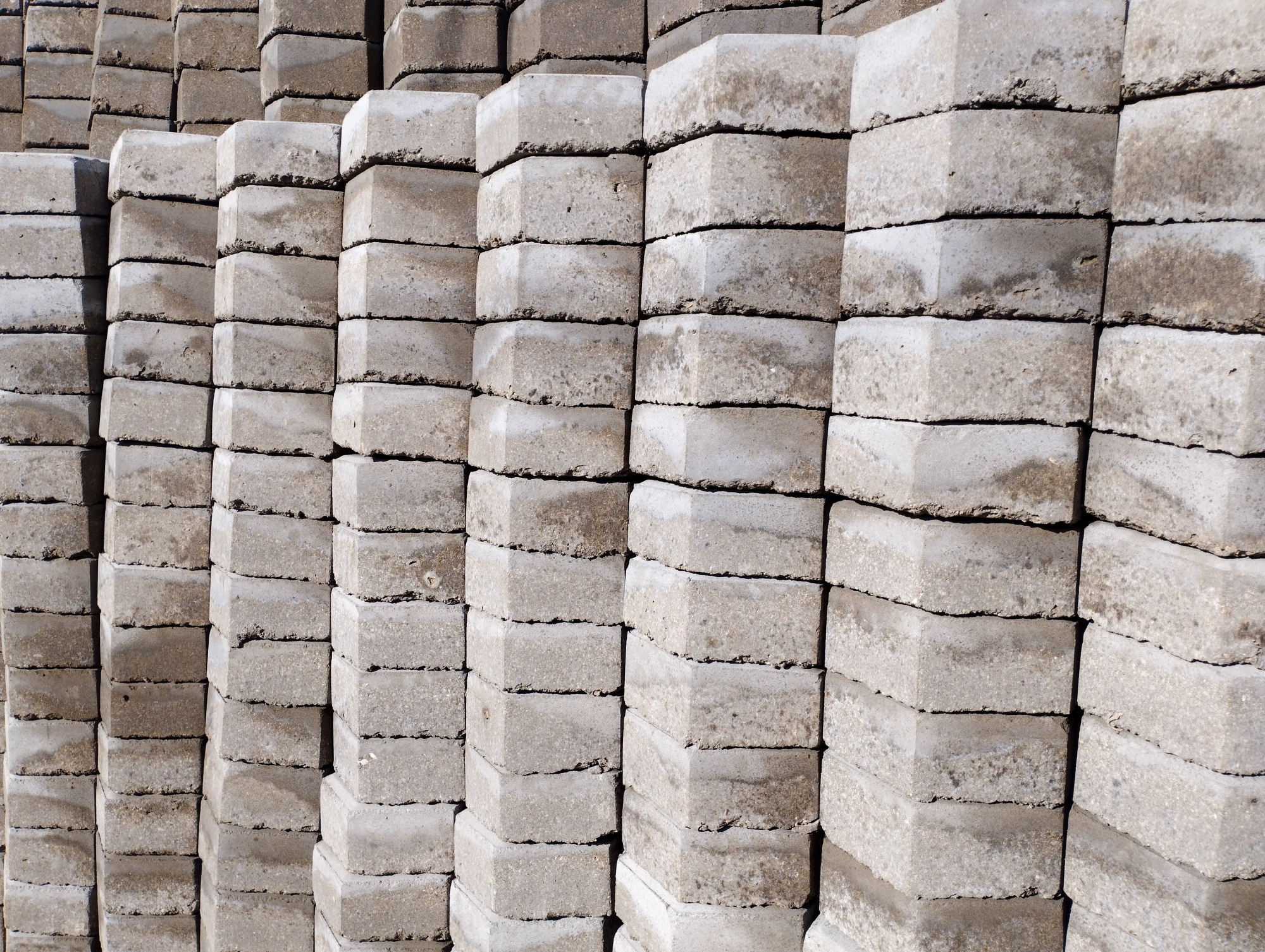 Rows of stacked gray concrete paving blocks with rough surfaces and layered textures