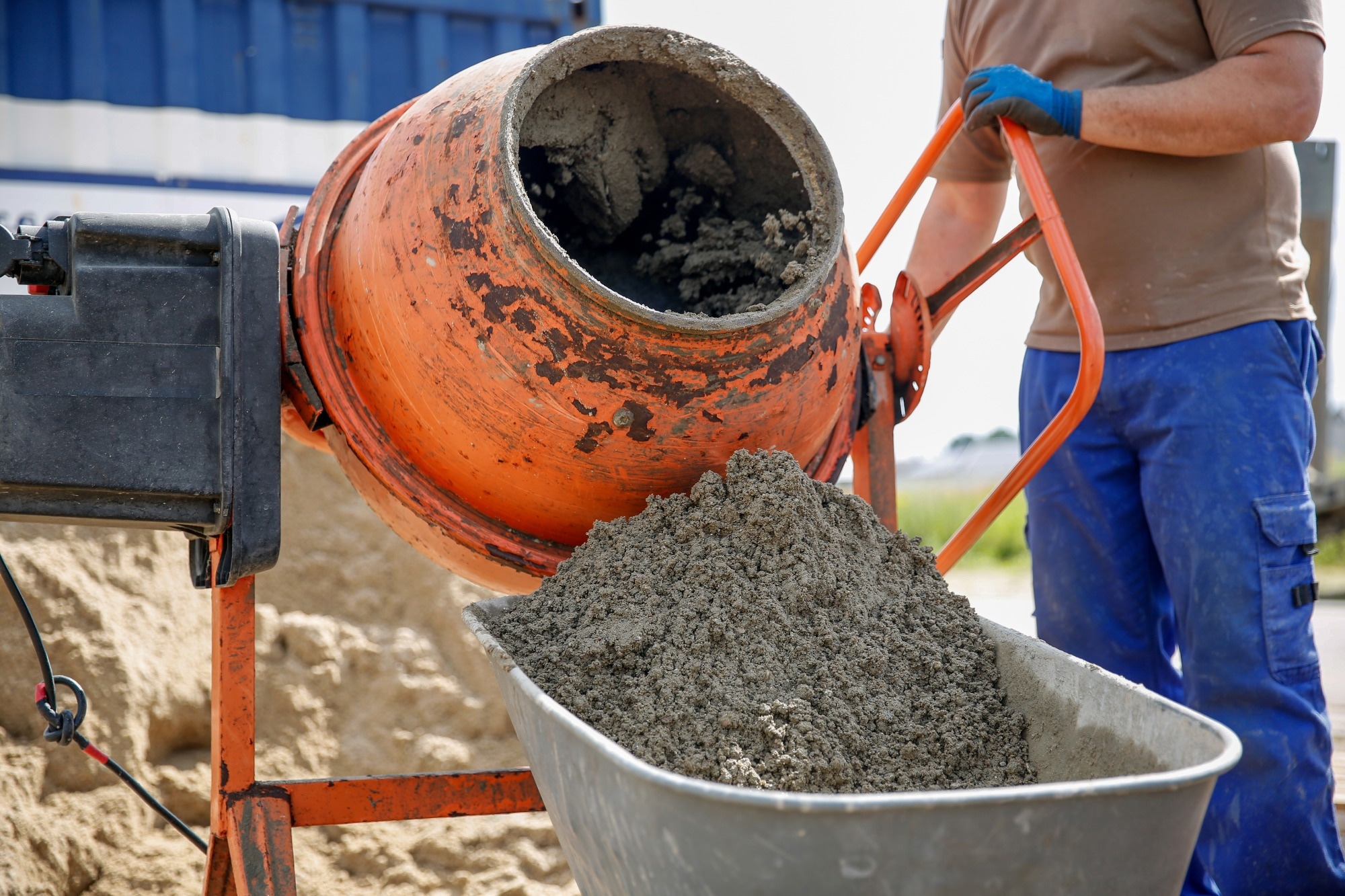 A construction worker mixes cement and pours it into a wheel barrow.