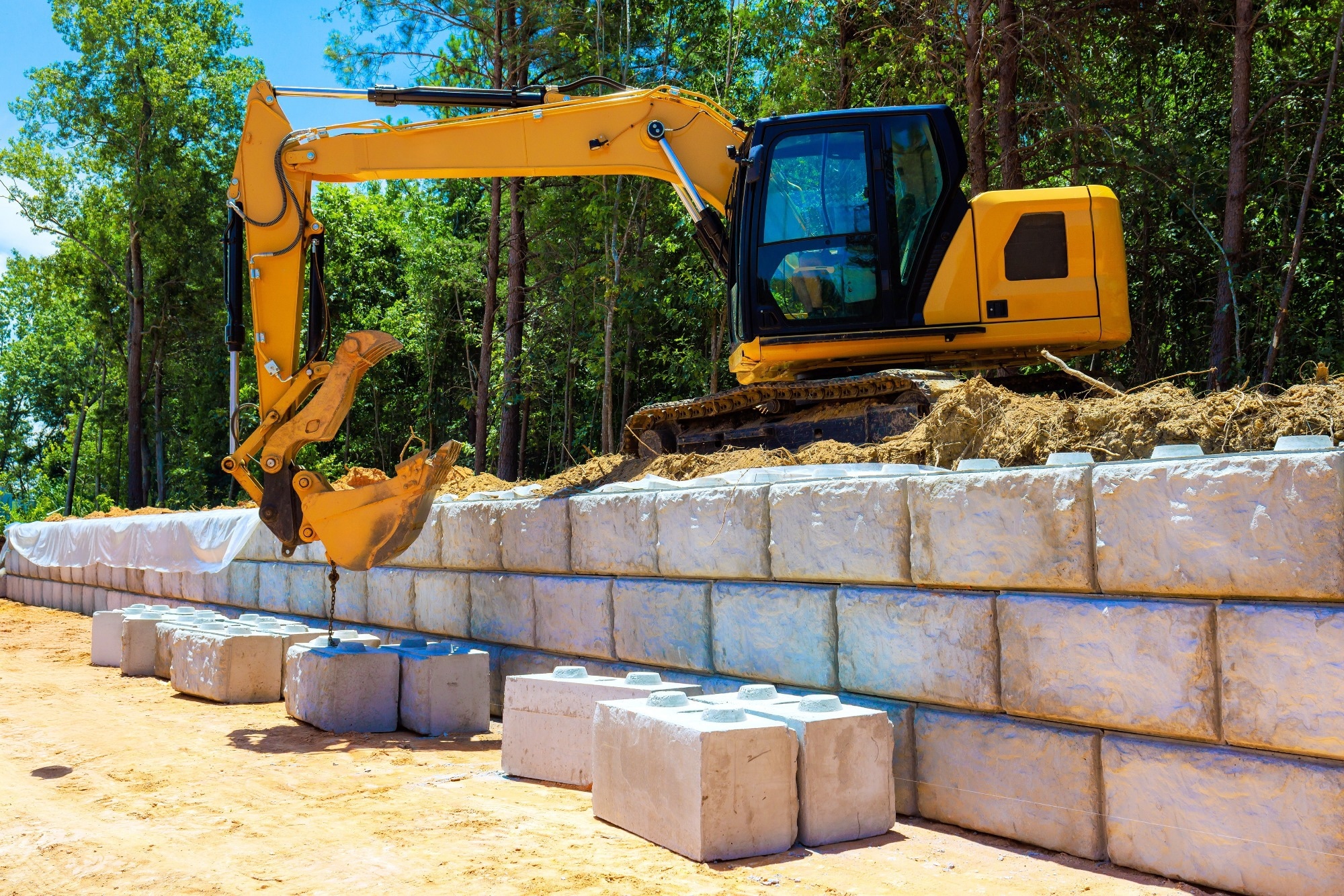 Heavy machinery is actively involved in constructing retaining wall using concrete blocks