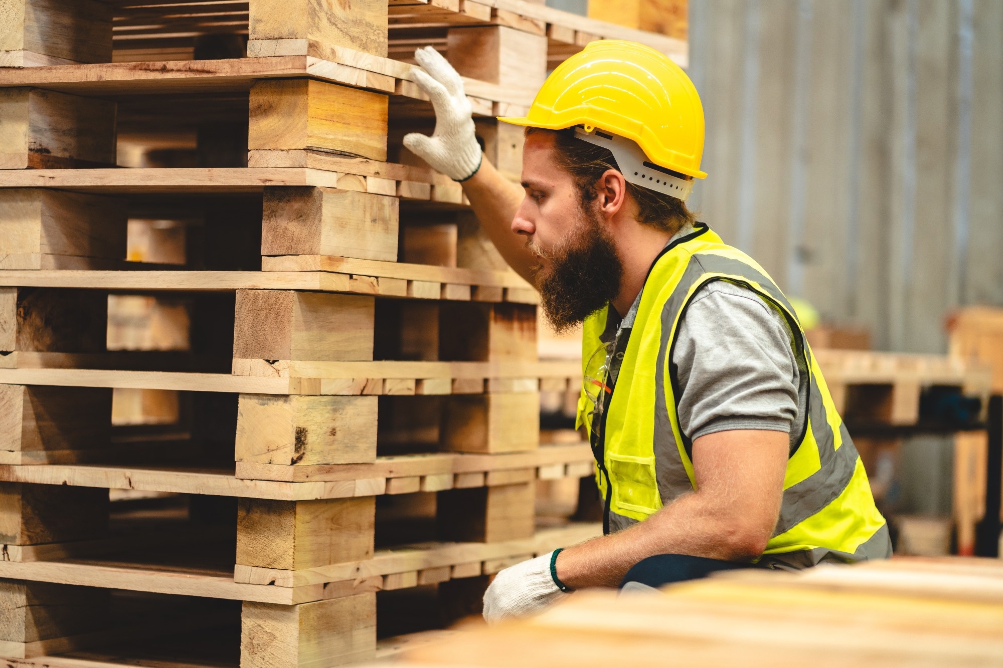 Man looking at a pile of wooden pallets in warehouse.