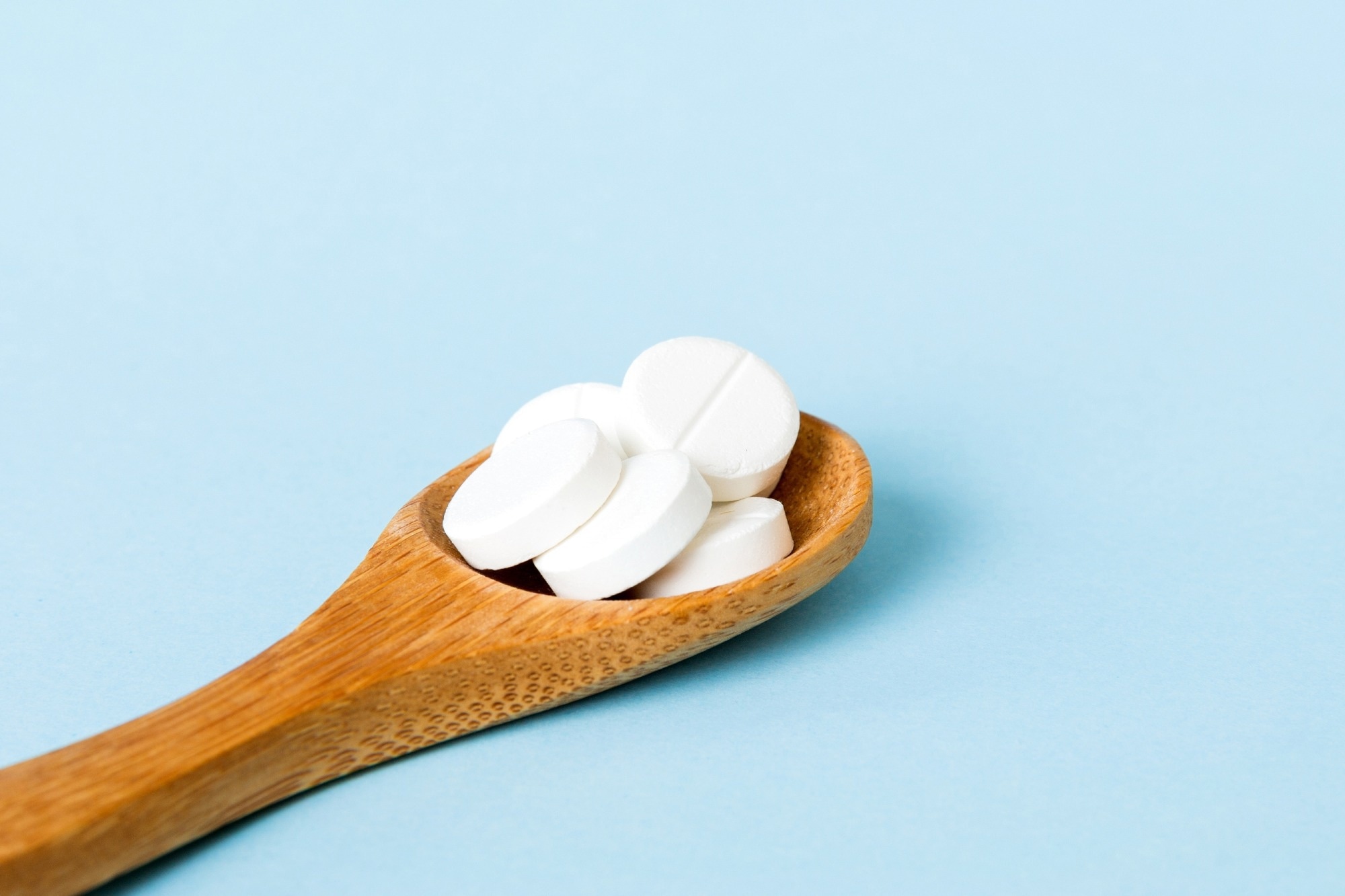 White chemical powder (Titanium dioxide, TiO2) on a wooden spoon on blue background.
