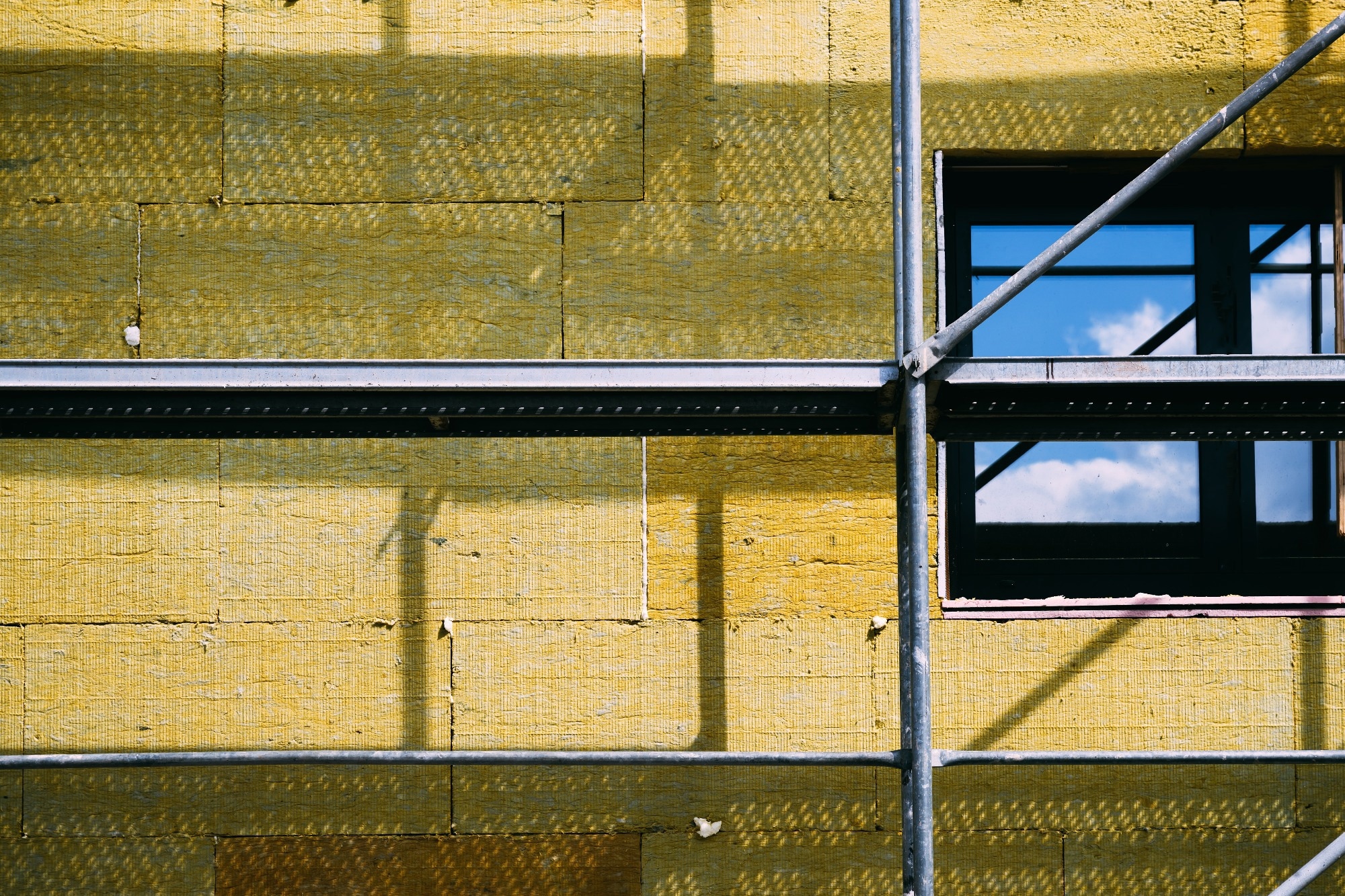 Construction site with scaffolding and high-density slab insulation product installation on building facade. Selective focus.