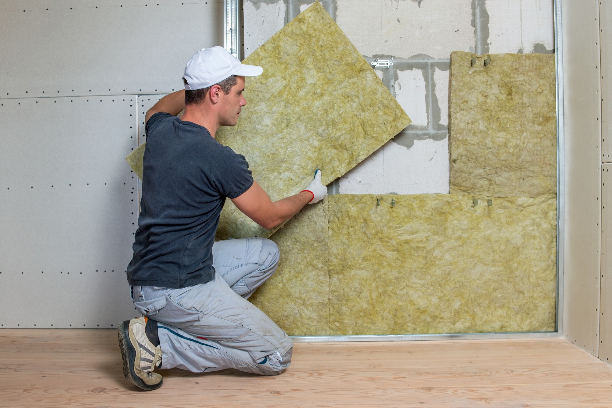 Worker insulating a room wall with mineral rock wool thermal insulation..