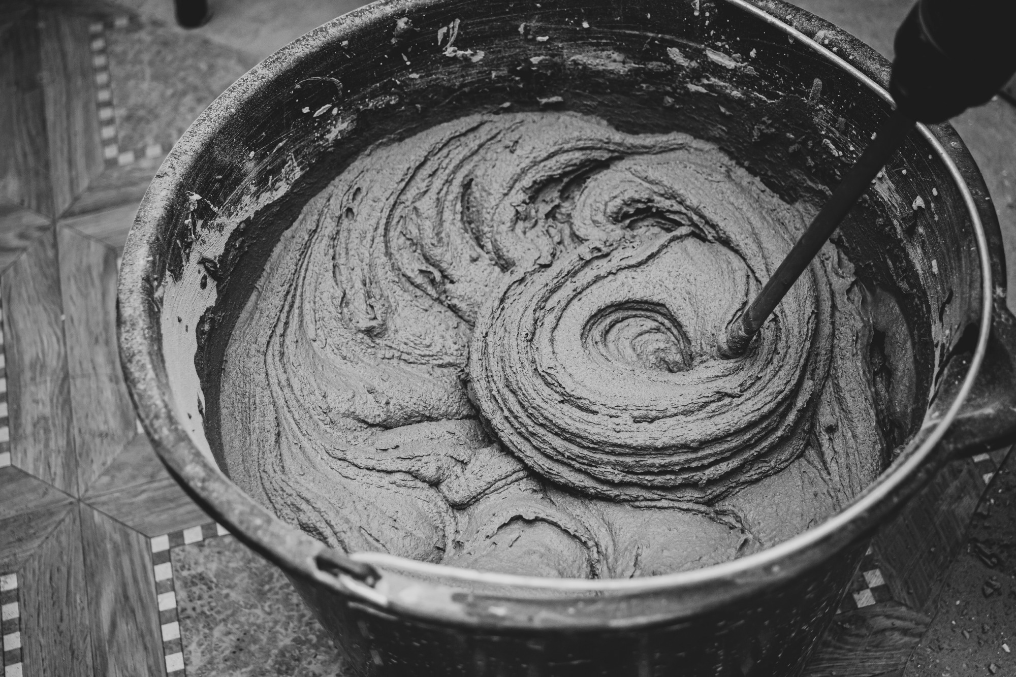 Mixing cement adhesive with a mixer in a bucket close-up.