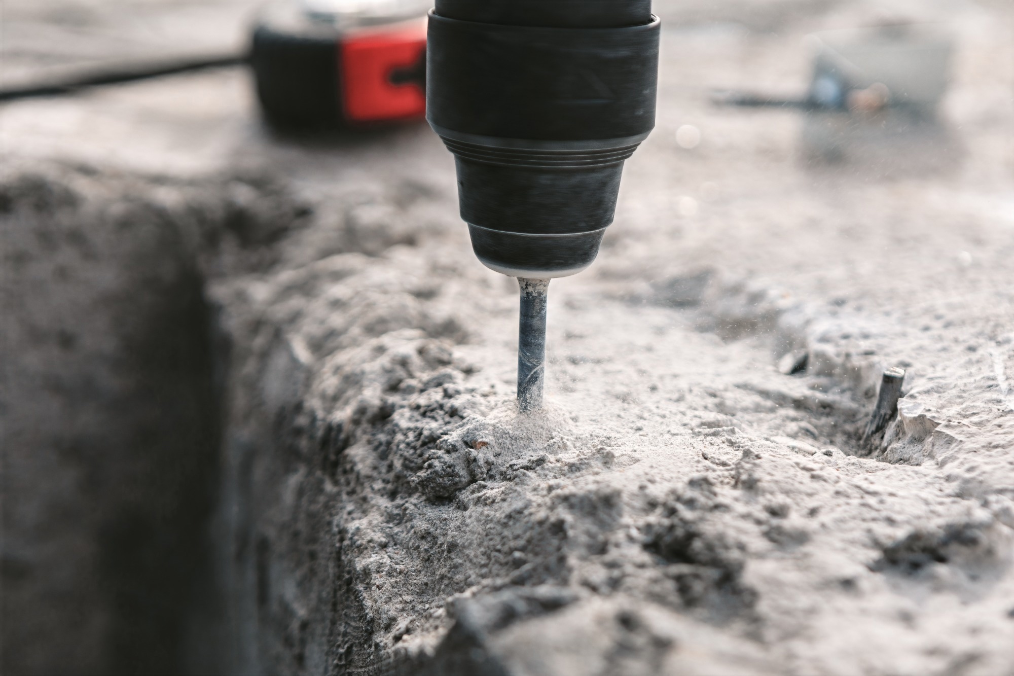 Concrete foundation is being reinforced with a powerful impact drill. Dust heap billow as the drill bit makes its way through the concrete wall